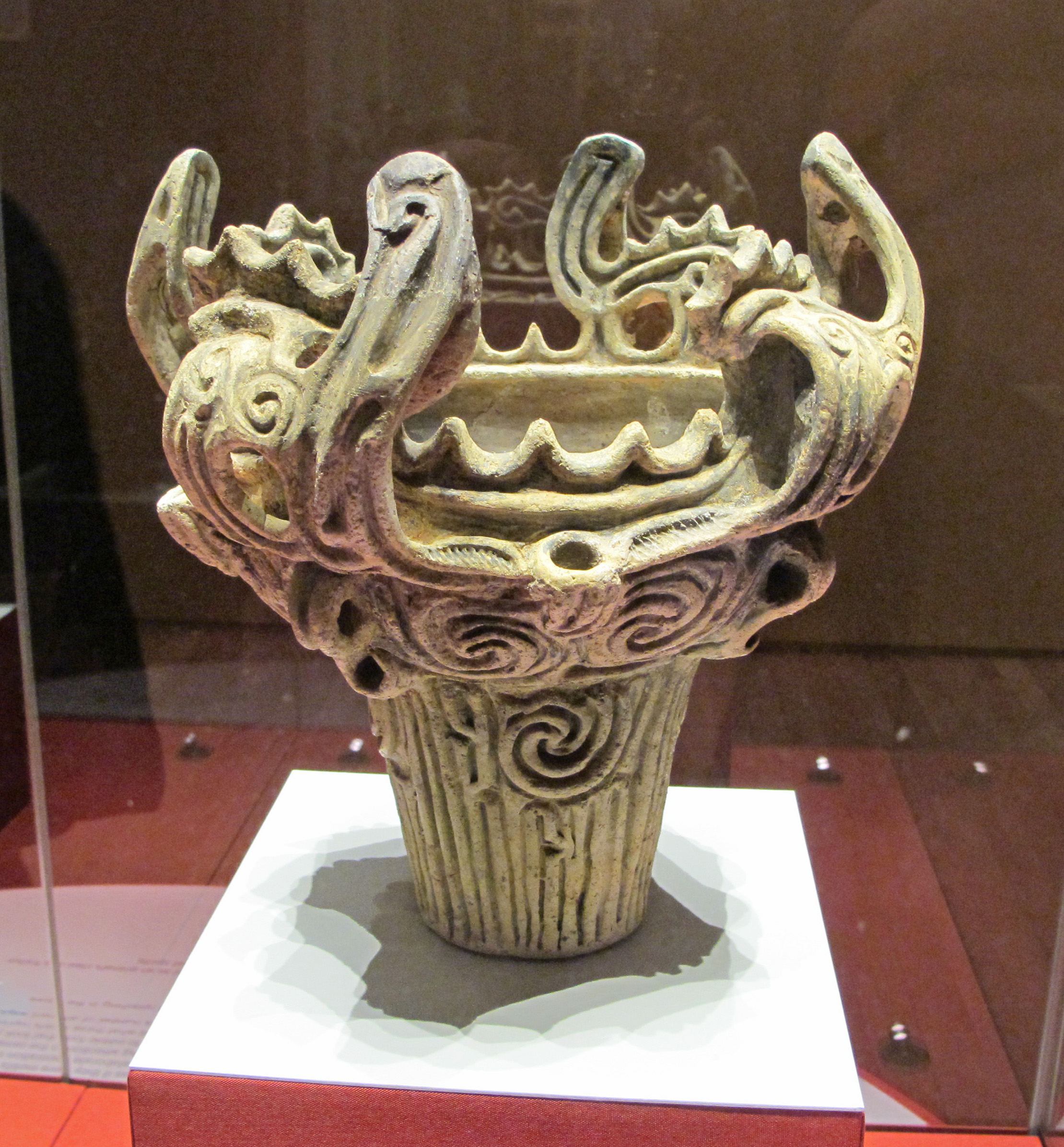 A pale Jōmon clay pot on display within a glass case at the British museum.