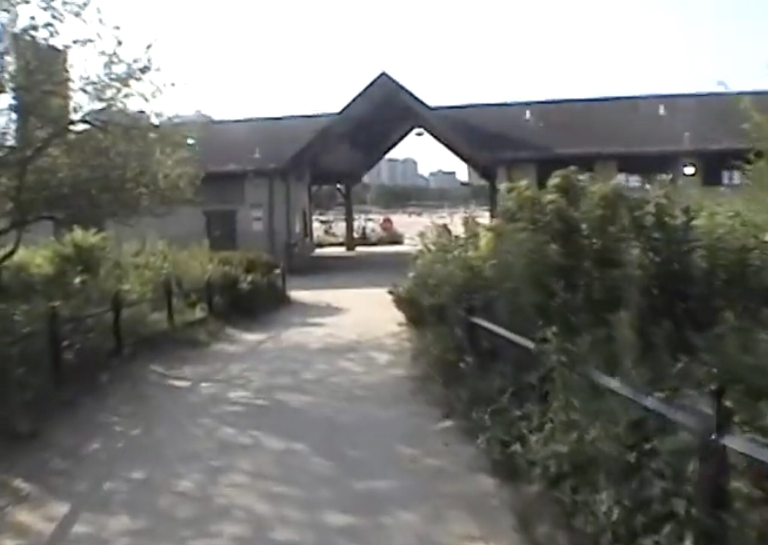Screenshot of a low-res digital video, looking from a trail toward a Lake Michigan beach through the breezeway of a field house.