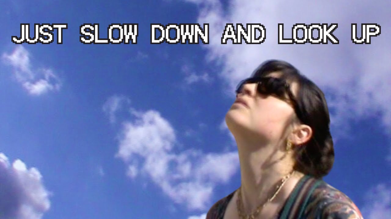 CQ Lucius in sunglasses, looking up at a cloudy blue sky overlaid with the title "Just Slow Down And Look Up."