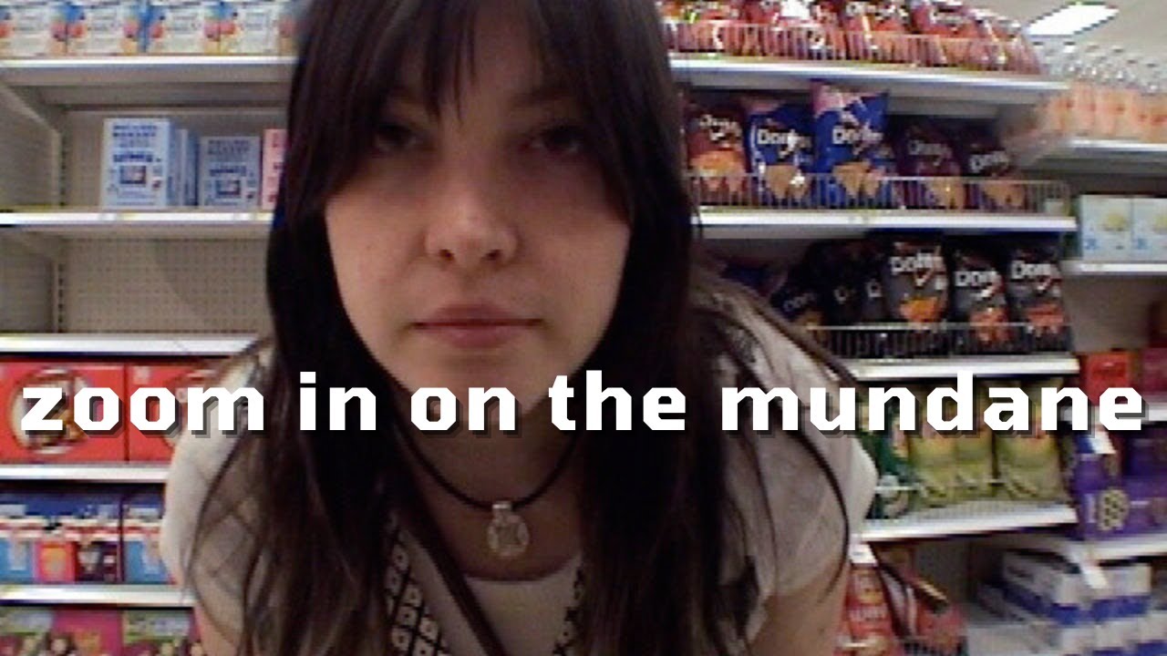 A video thumbnail of Lucius looking into the camcorder lens, standing in a grocery-store chip aisle, entitled "zoom in on the mundane."