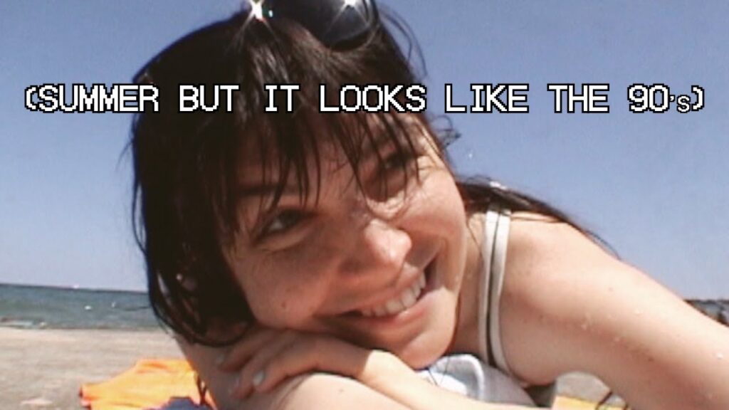 A digital camcorder screenshot of CQ Lucius lying on a beach towel, entitled "(Summer But It Looks Like The 90s)."