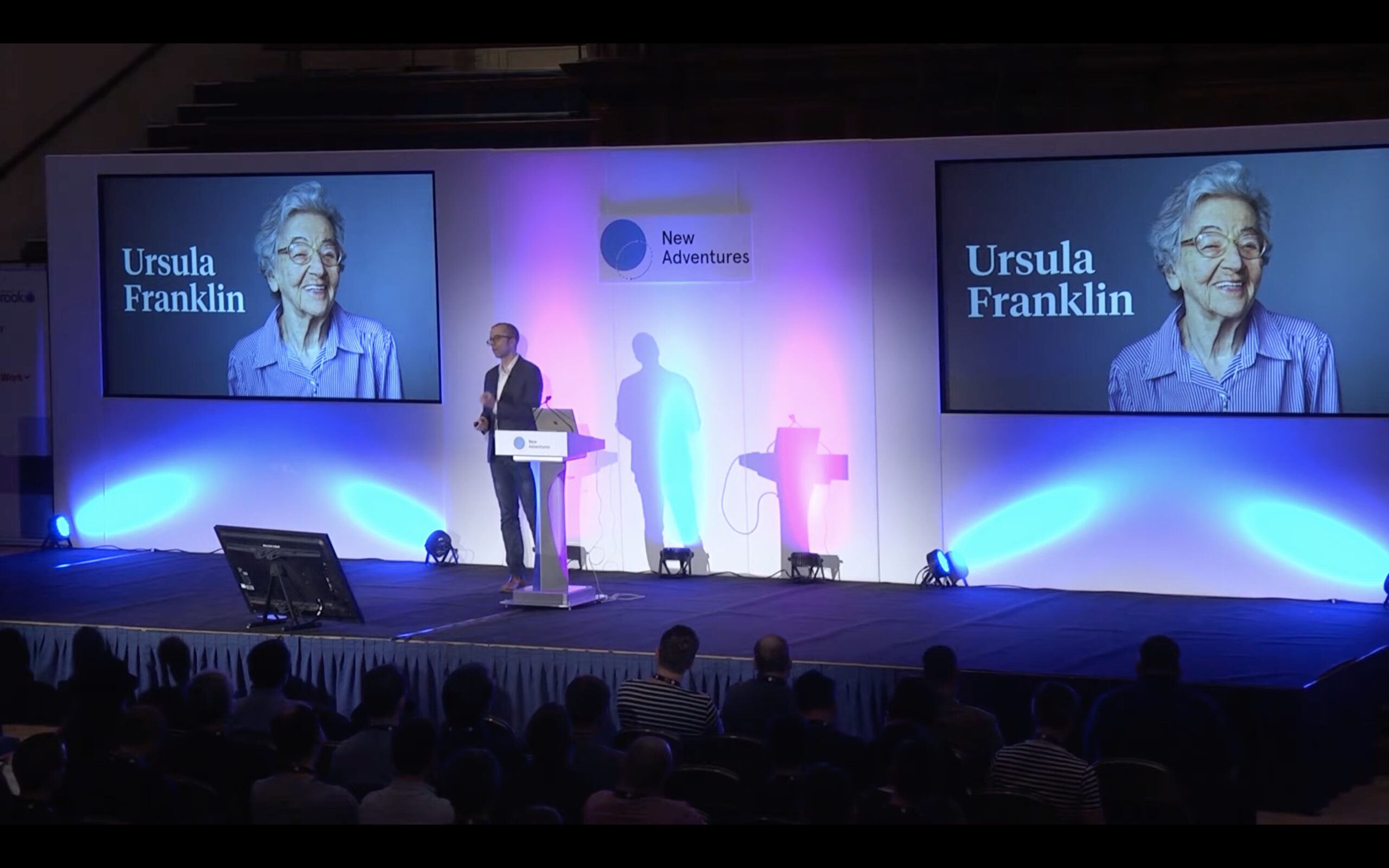 Ethan giving a talk at the New Adventures conference, on a stage with slides showing Ursula Franklin on either side of him.