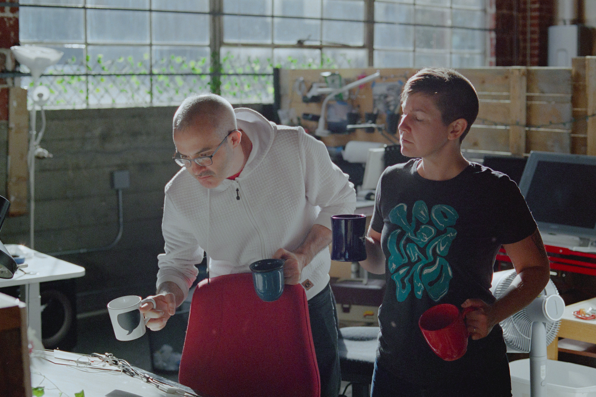 Matt and Erika, looking sternly down at a drafting table in Helioscope Studio while holding a total of four coffee mugs.