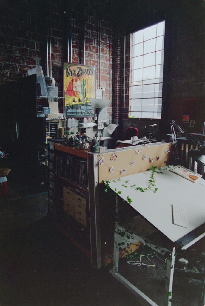 The interior of Helioscope Studio, with several individually decorated drafting tables lit by a tall industrial window.
